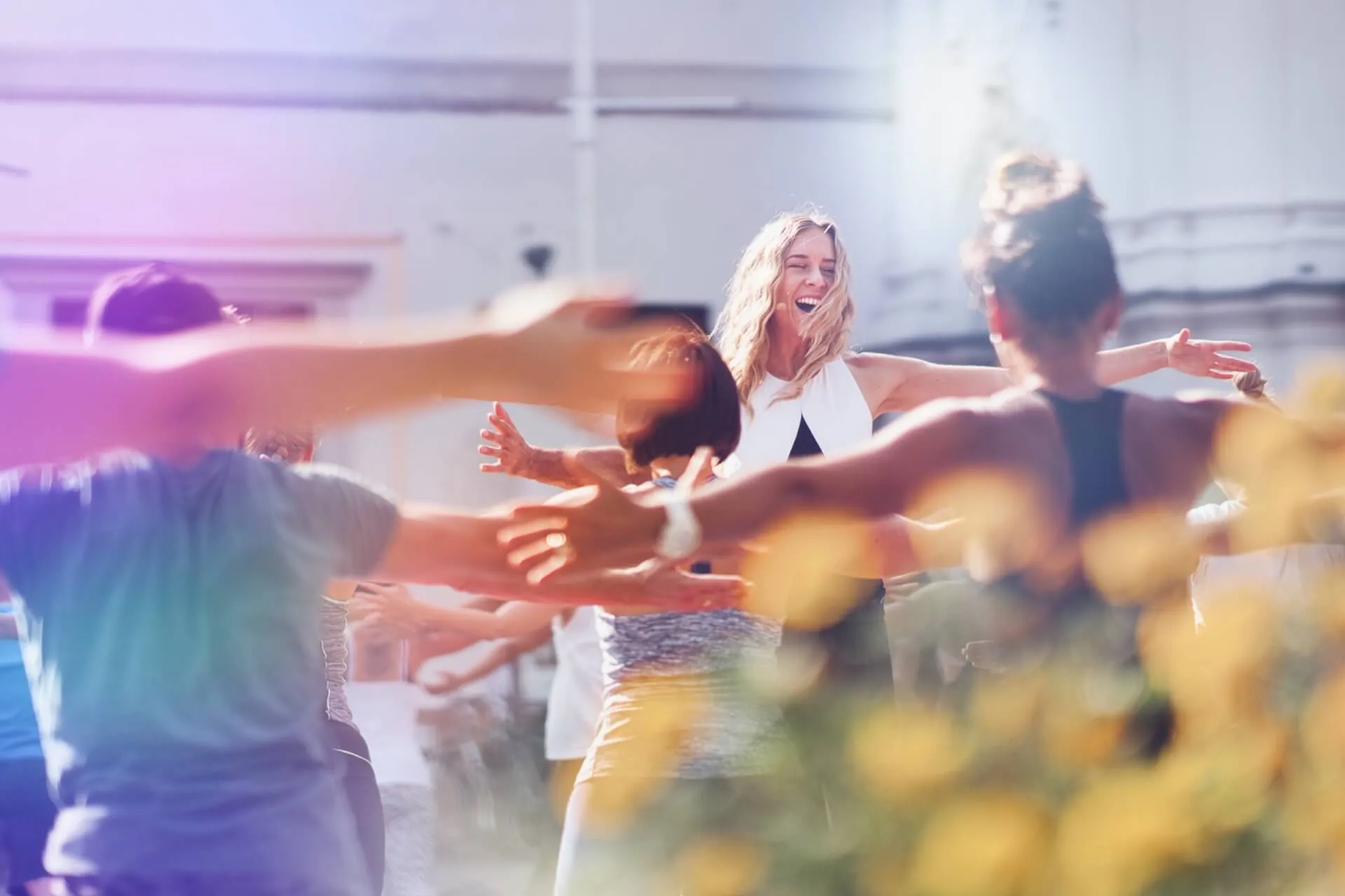 Suzanne lacht inmitten einer Gruppe mit ausgestreckten Armen, warmes goldenes Licht