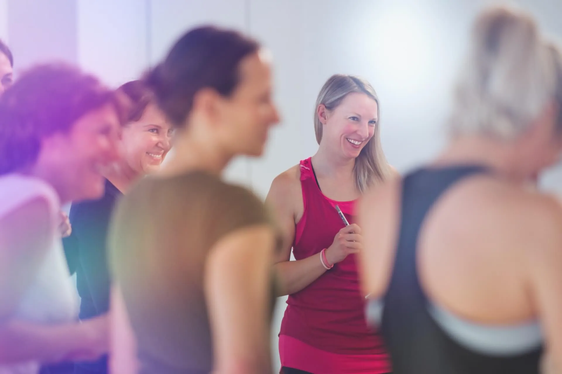 Trainerin in pinkem Top mit Stift, lachend inmitten einer Gruppe